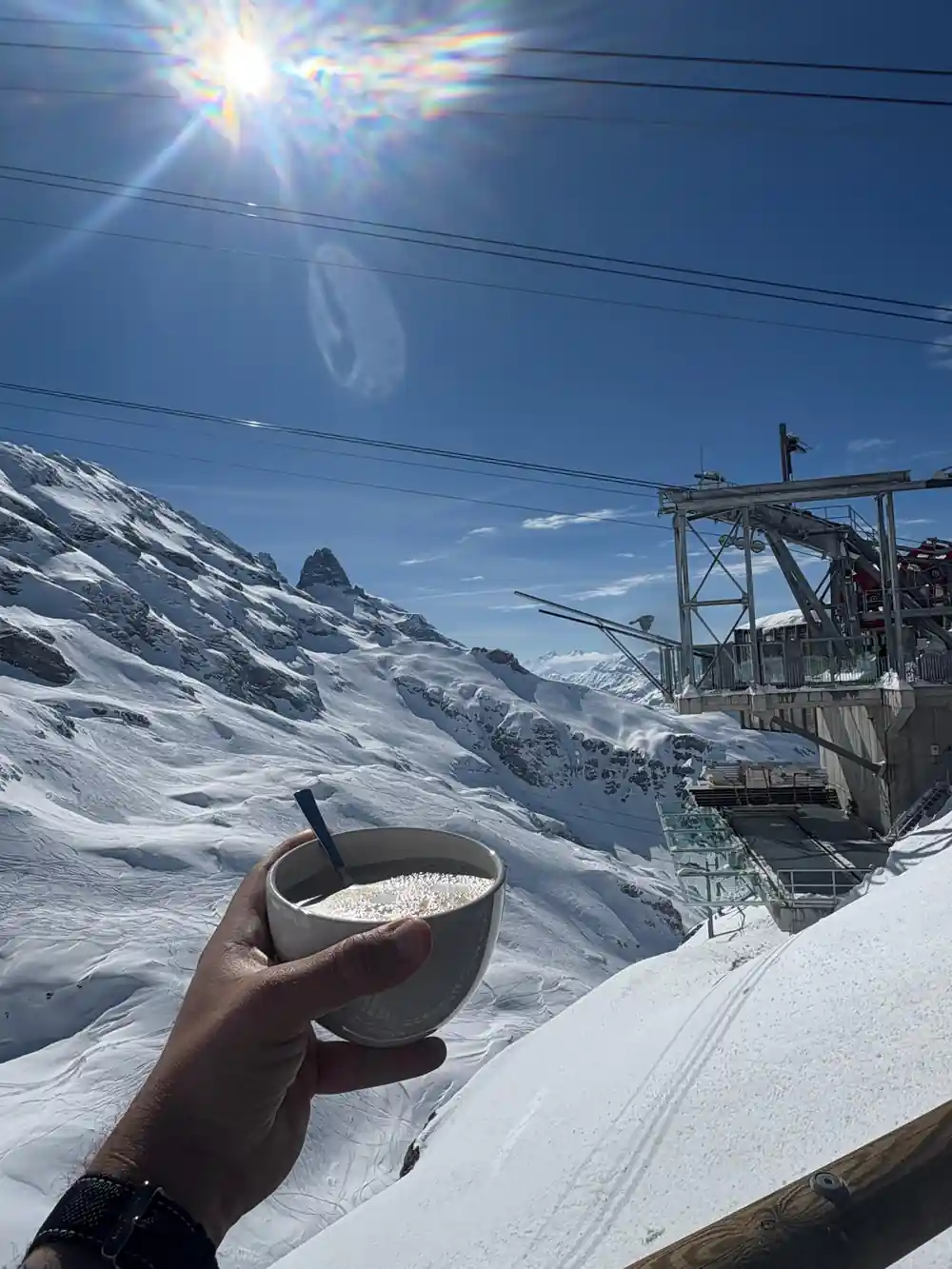 A cup of coffee held up against the snow and the cable car station