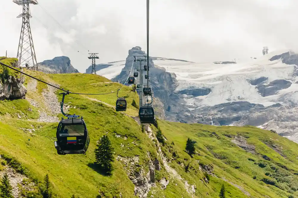 Gondolas climbing a green slope with the glacier behind