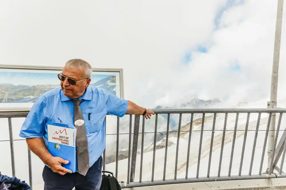 The guide waiting at a railing with the tour folder under his arm