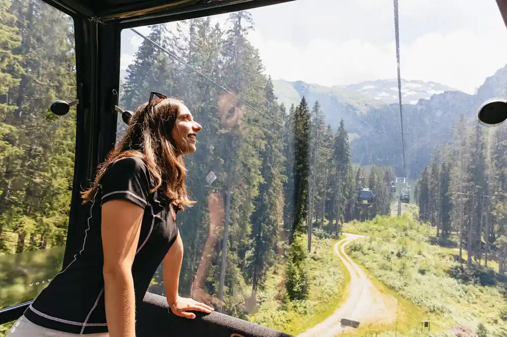 A passenger looking out of the cable car at the forested valley