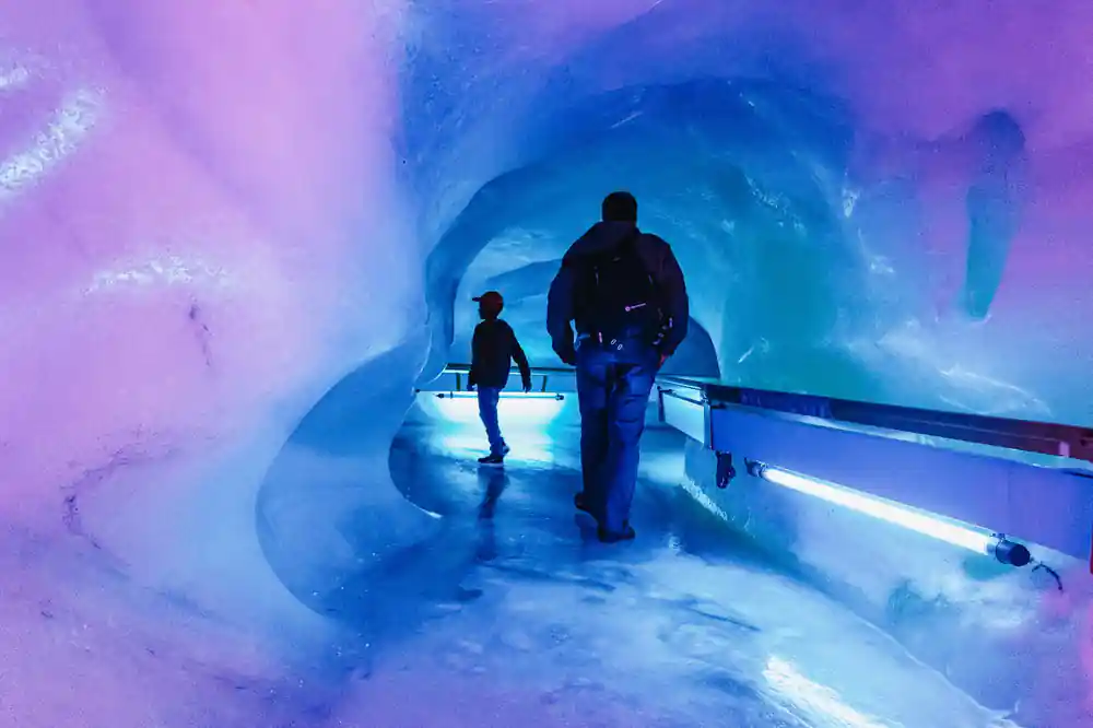 Two visitors walking through the blue-lit tunnel of the glacier cave