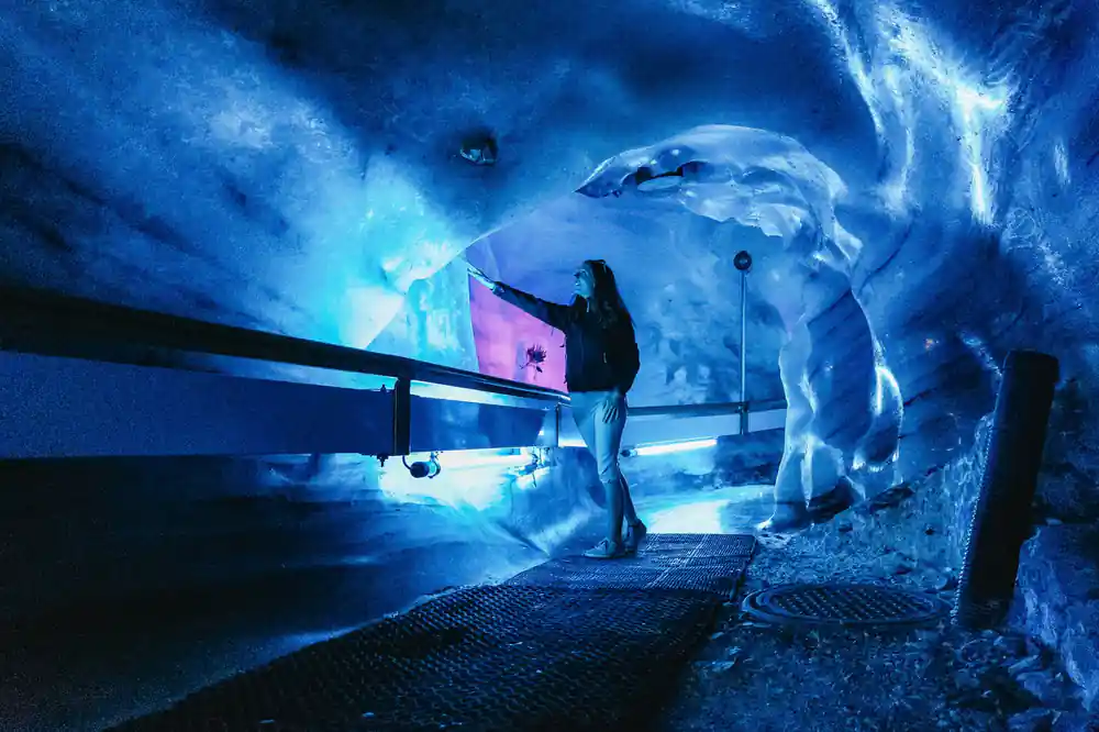 A visitor with a hand on the lit ice wall of the cave