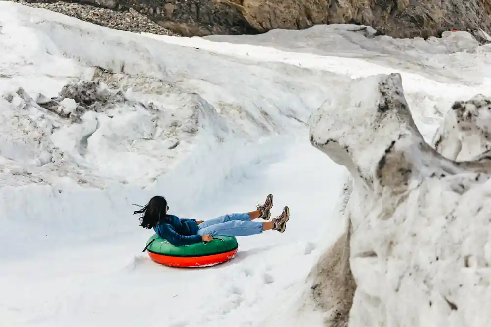 A visitor on a red and green snow tube in a hollow of the glacier